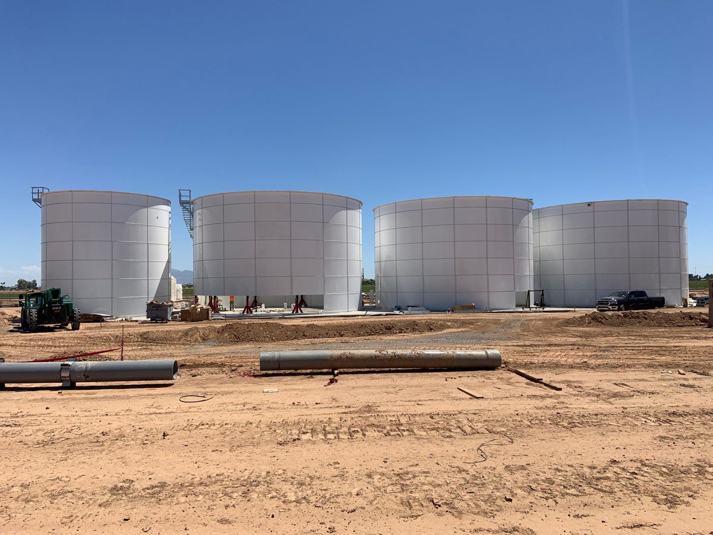 Four bolted steel storage tanks under construction on a prepared site