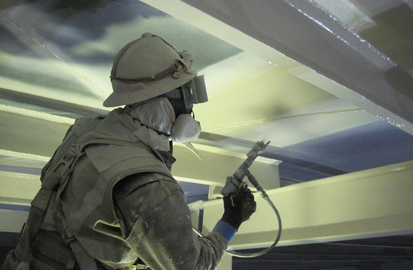 Worker in protective gear spray-applying a new lining to the interior steel of a tank