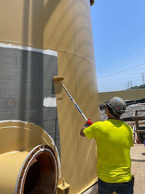 Worker rolling a new protective coating onto a prepared tank exterior