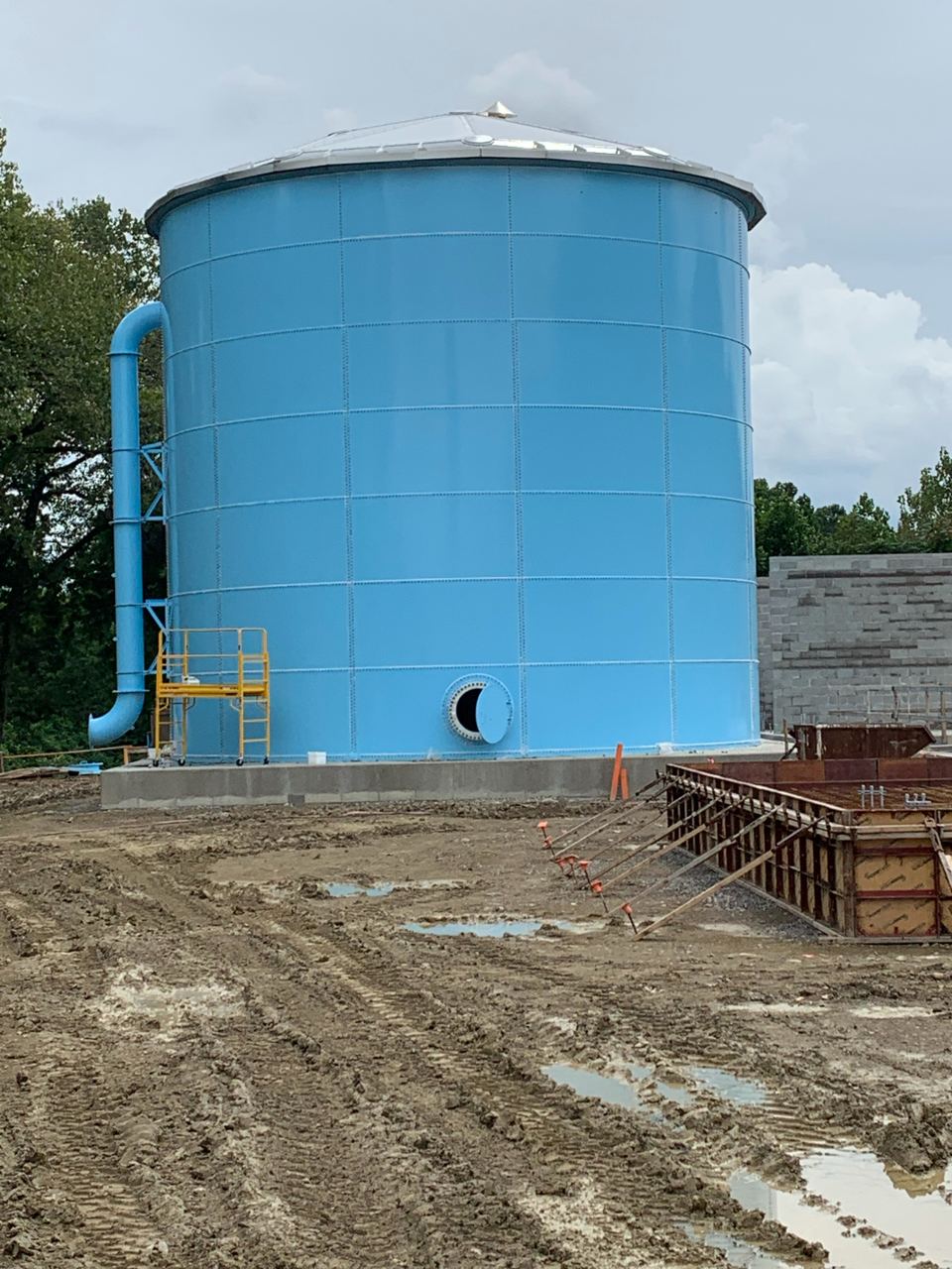 Blue glass-fused-to-steel bolted tank with side manway and inlet piping on a poured ring-wall foundation