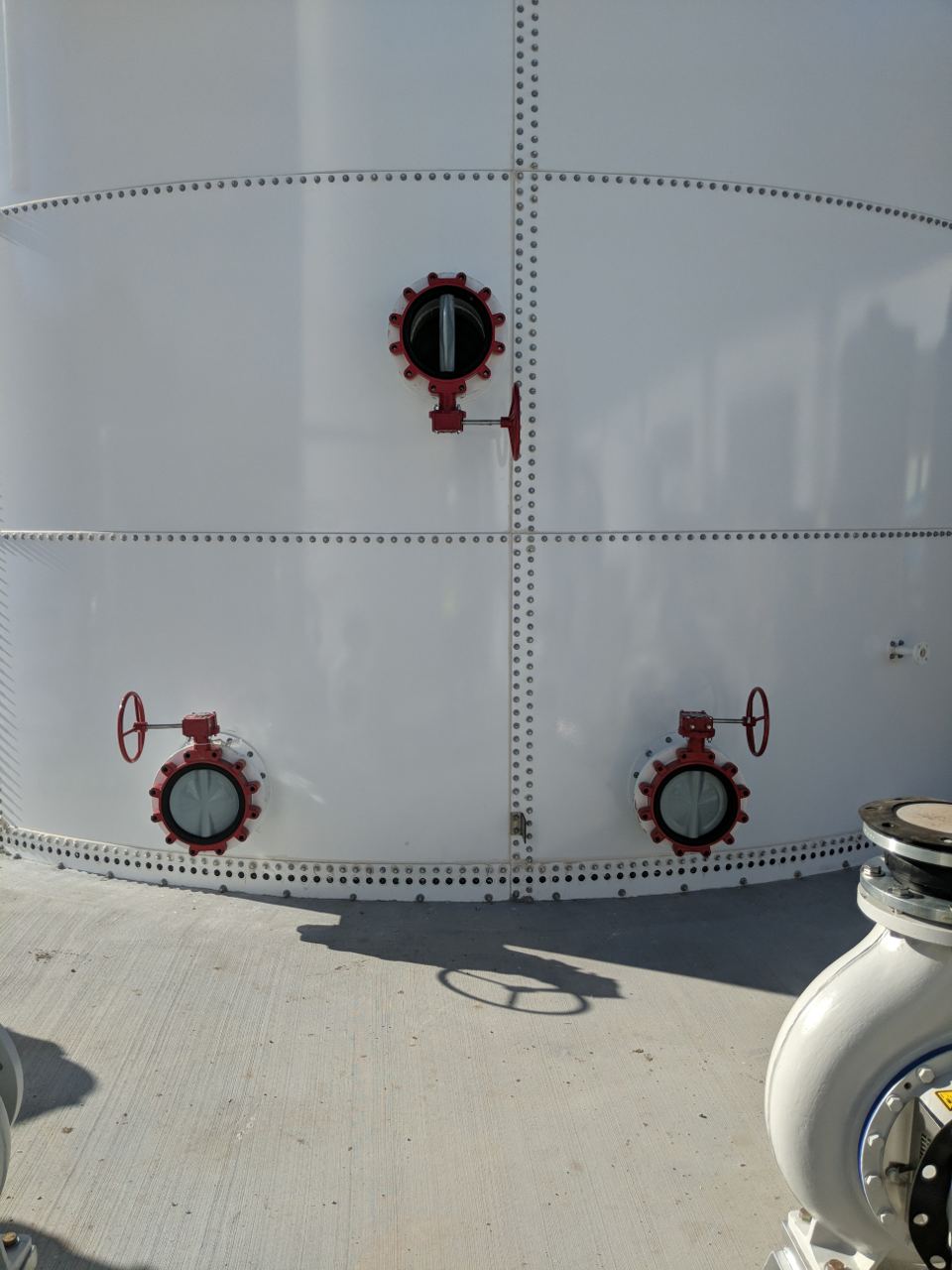 Close-up of red butterfly valves mounted on the white bolted panel wall of a steel tank