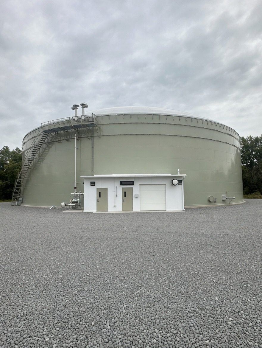 Sage-green bolted steel water tank with a low aluminum dome and an attached concrete valve house