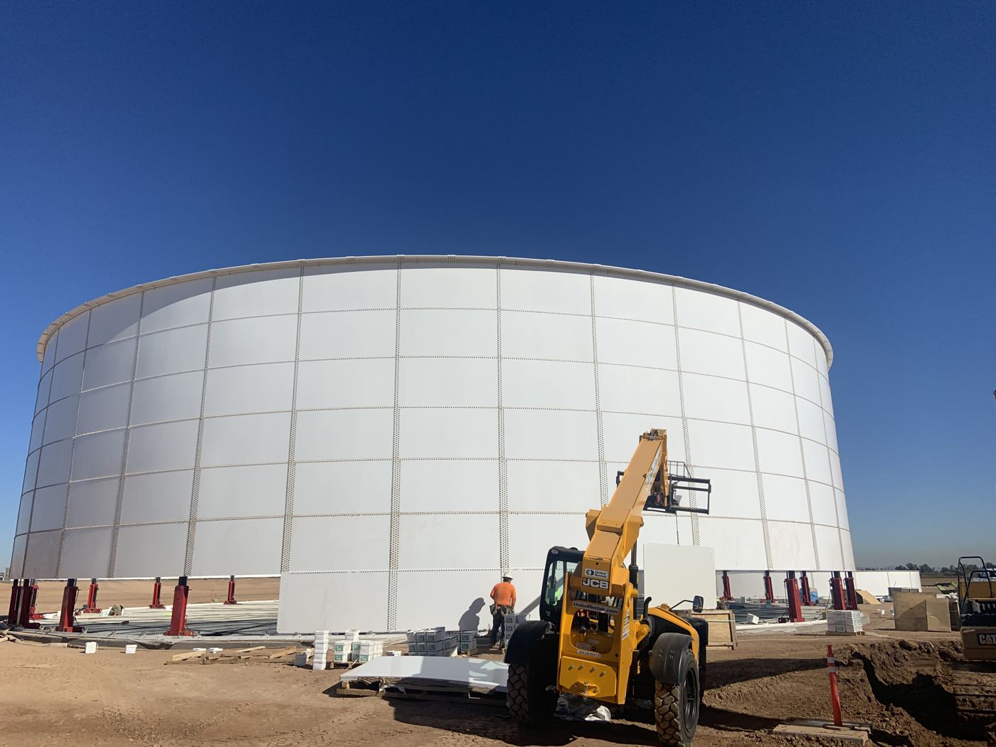 Large bolted steel tank raised on hydraulic jacks during ground-level erection