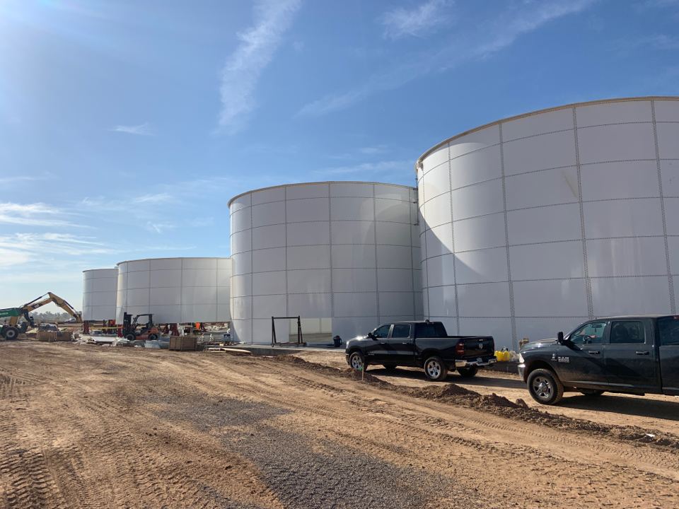 Row of white bolted steel tanks on a jobsite with crew trucks in the foreground