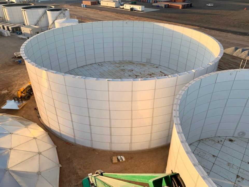 Overhead view into two open-top white bolted steel tanks under construction