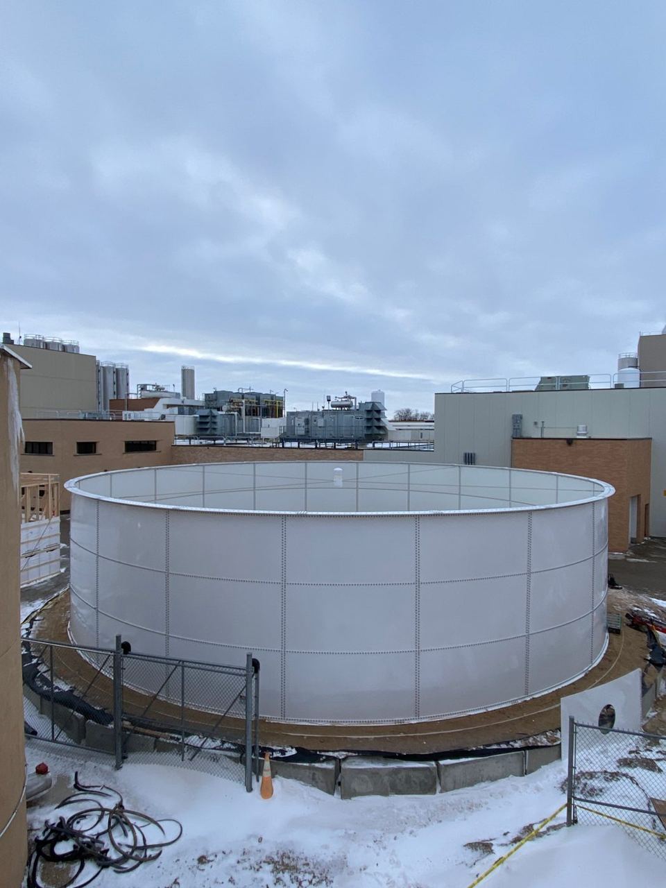 Open-top white bolted steel tank installed on an urban rooftop in winter