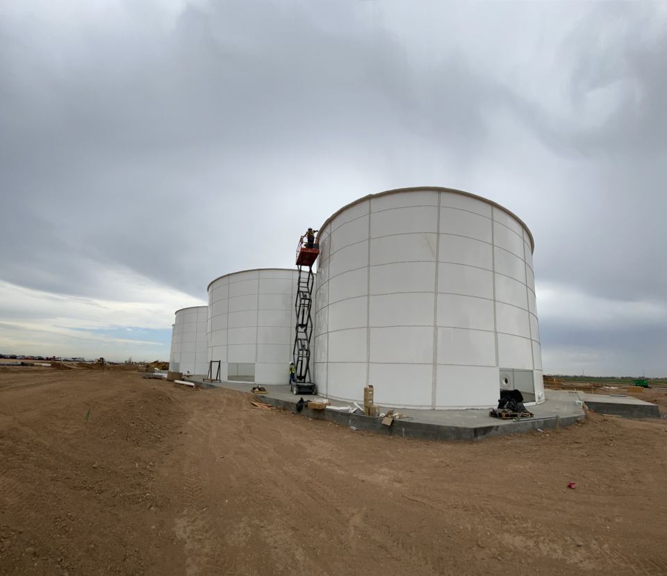 Three white bolted steel tanks under construction on ring-wall foundations