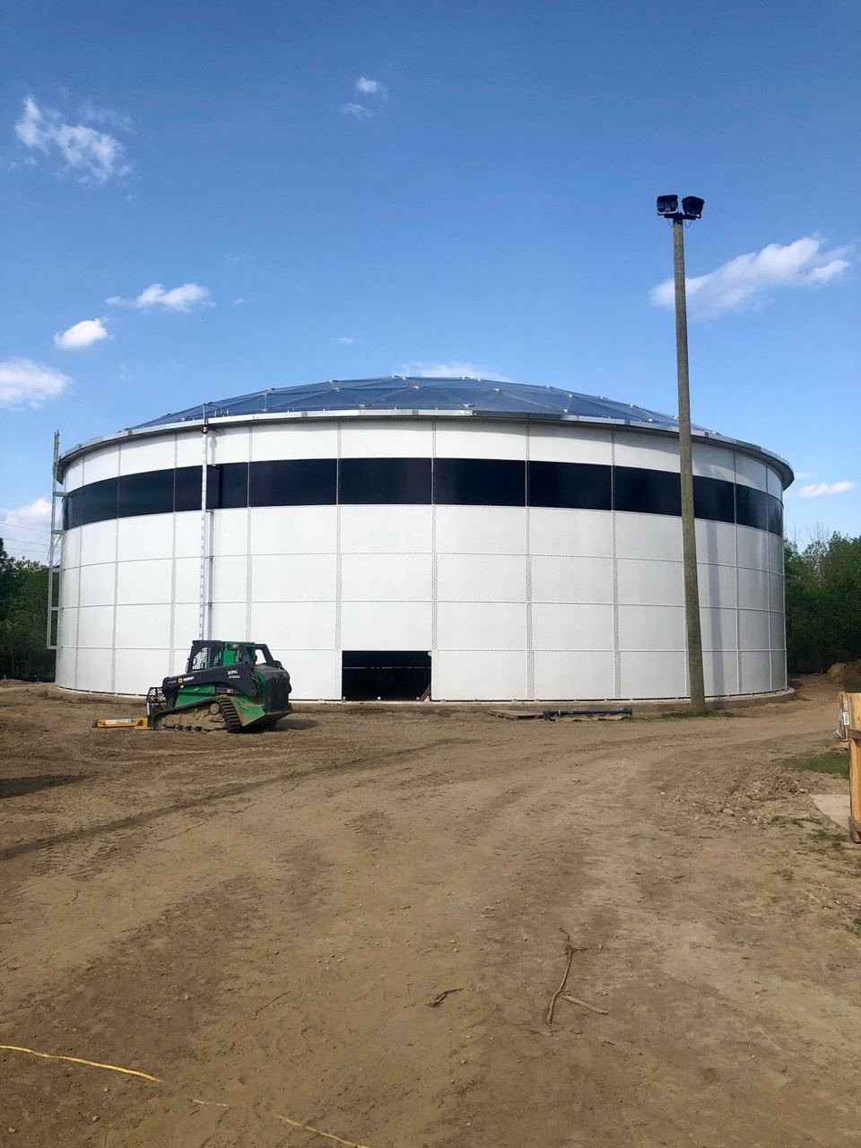 White bolted steel tank with aluminum dome roof and a telehandler working at its base during construction