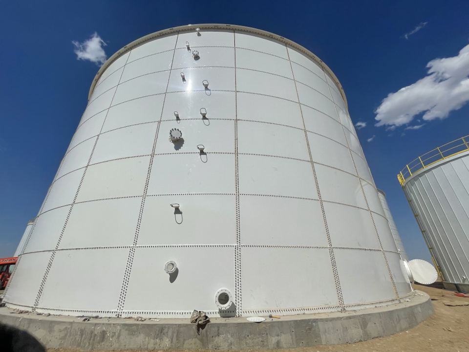 Wide view of a large white bolted steel tank with staged shell nozzles and fittings on the panels