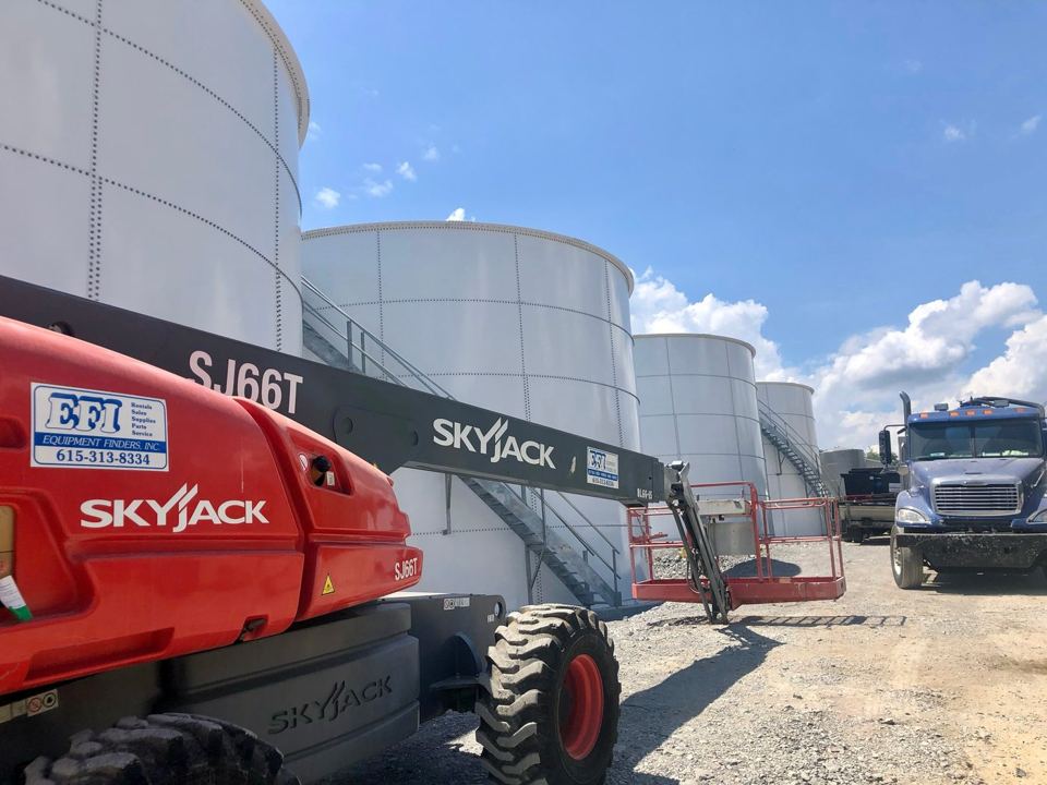Row of white bolted steel tanks staged in the yard with a telescopic boom lift in the foreground