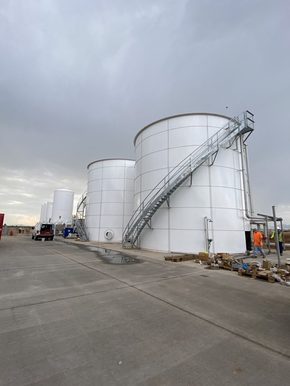 Row of white bolted steel tanks under construction on a paved fabrication yard