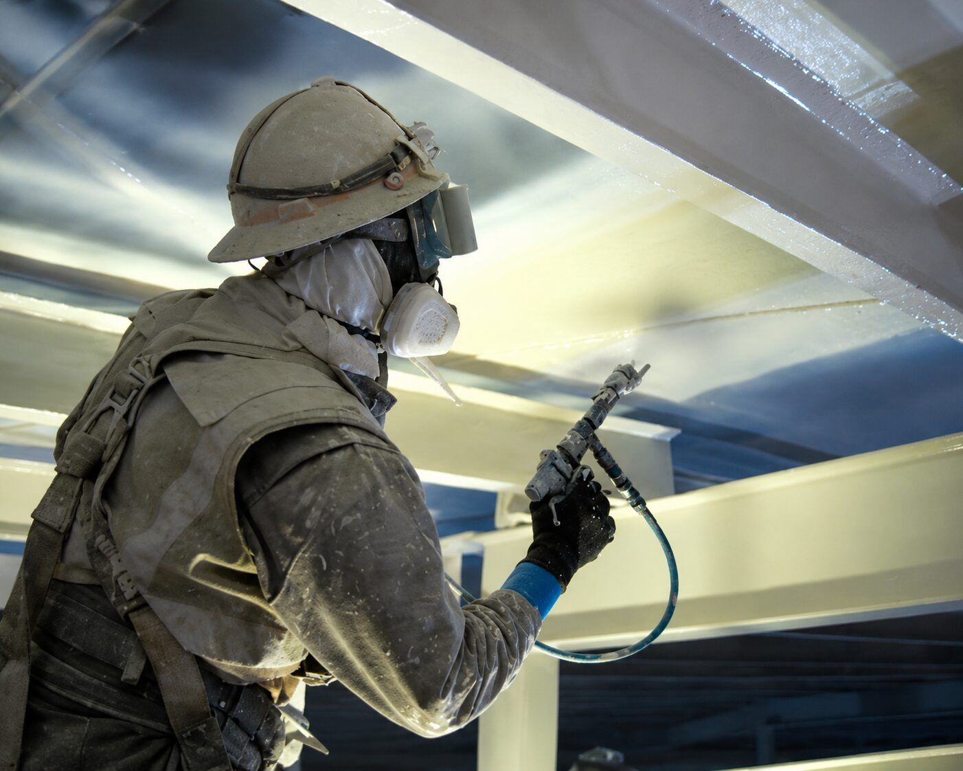 Protective coating being spray-applied to steel tank framing in a controlled work area