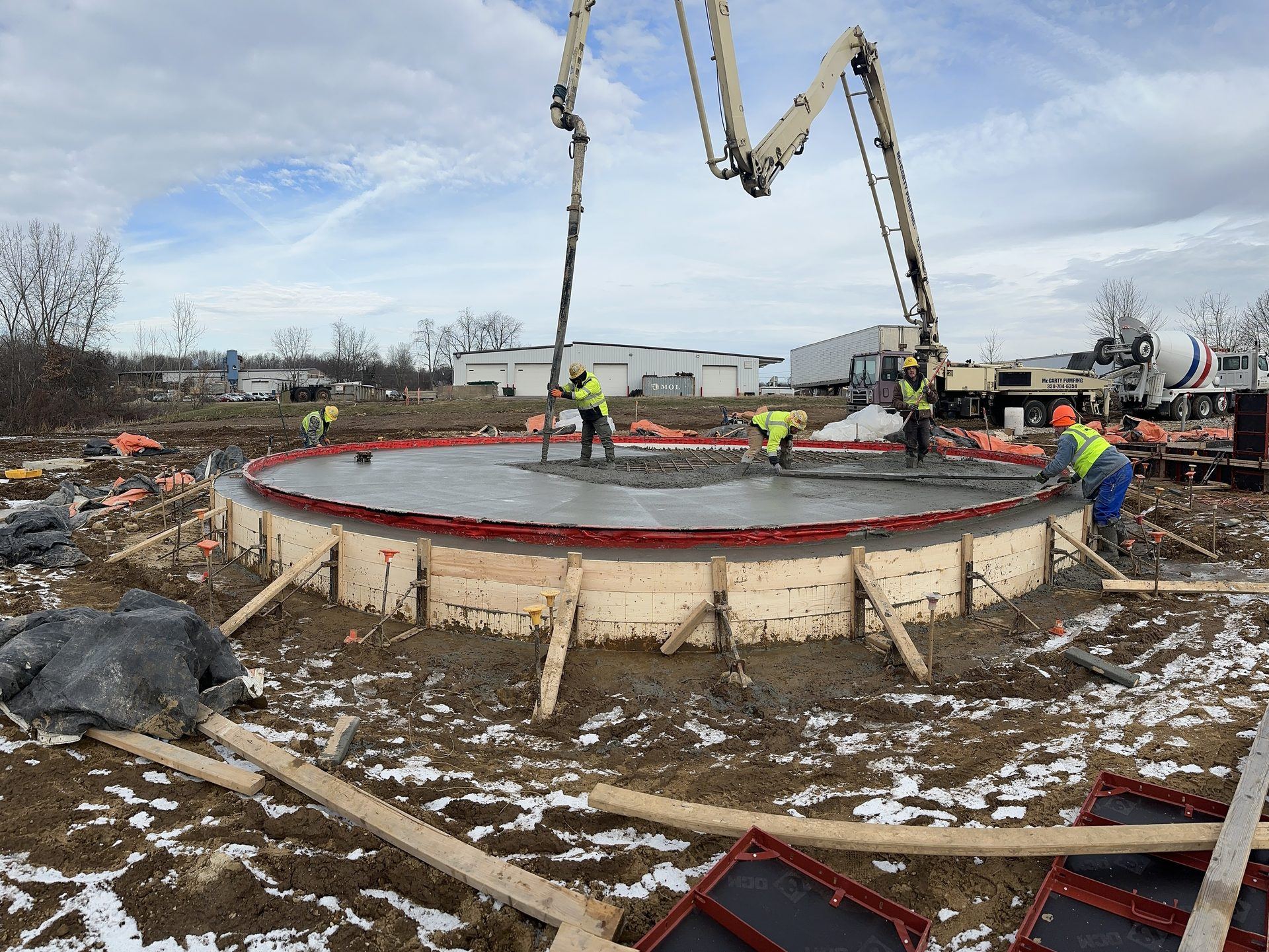 Crew pouring a circular concrete tank foundation with a boom pump
