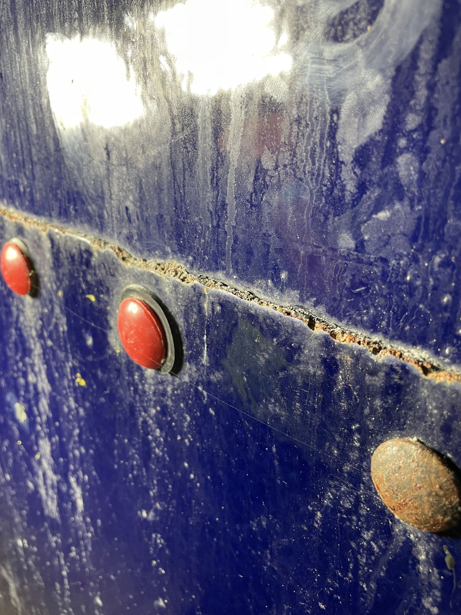 Cracked corroded seam line and bolt cap on a blue coated tank panel