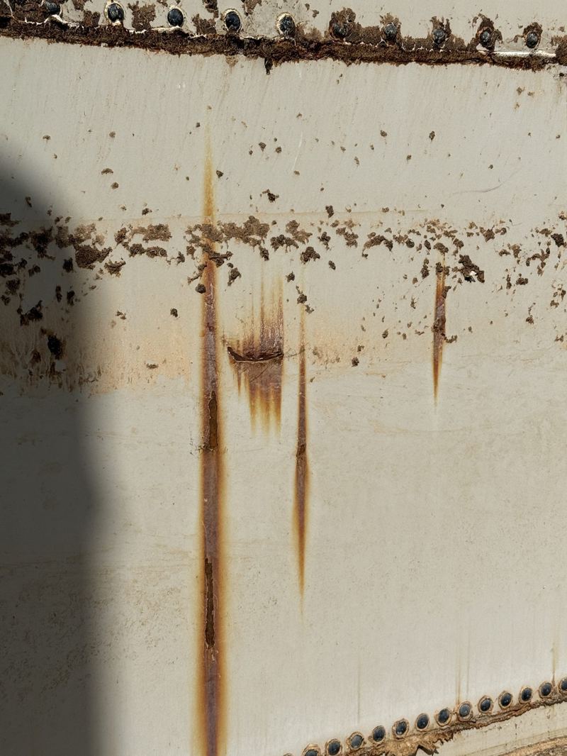 Pitting and rust streaking down a tank shell where splash- and vapor-zone exposure accelerated corrosion