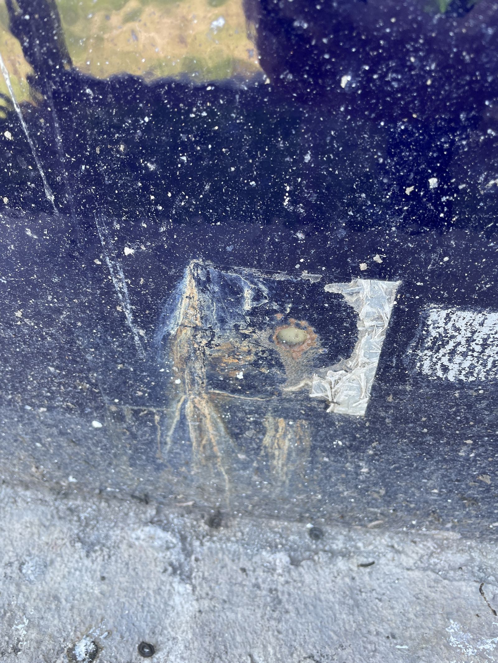 Pitting and corrosion at a tank detail photographed against a concrete surface