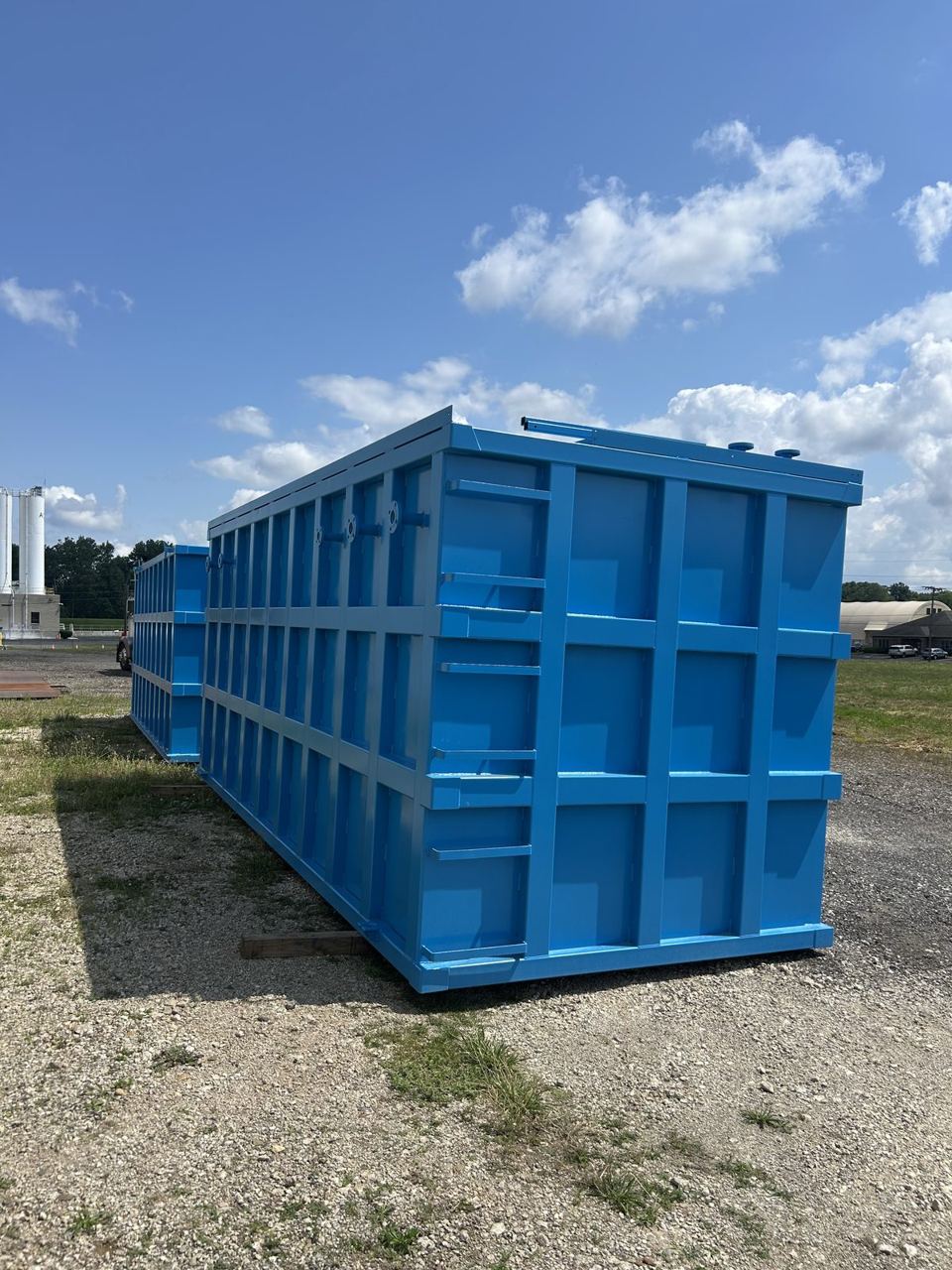 Long bright blue modular steel tank in three-quarter perspective with top-edge nozzles and a reinforced panel grid running its full length outdoors