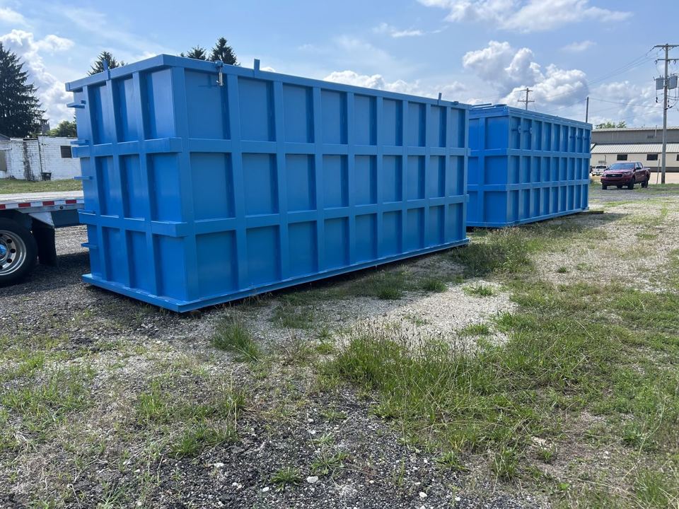 Pair of bright blue open-top modular steel tanks staged side by side in a grassy yard, externally reinforced panel walls under a clear sky