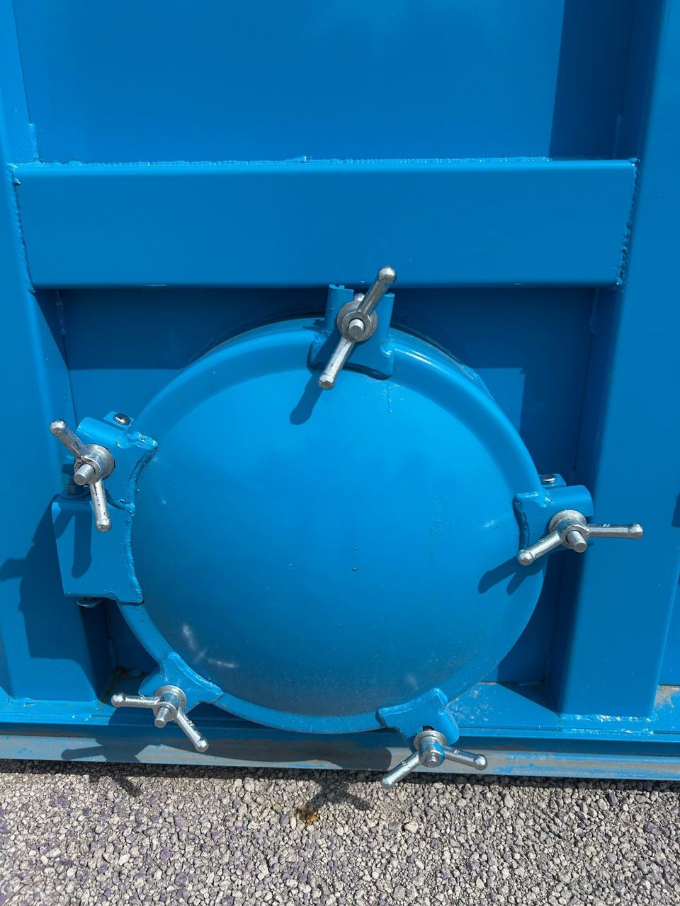Close-up of a bolted circular manway cover secured with wing-nut clamps on a bright blue modular steel tank in sunlight