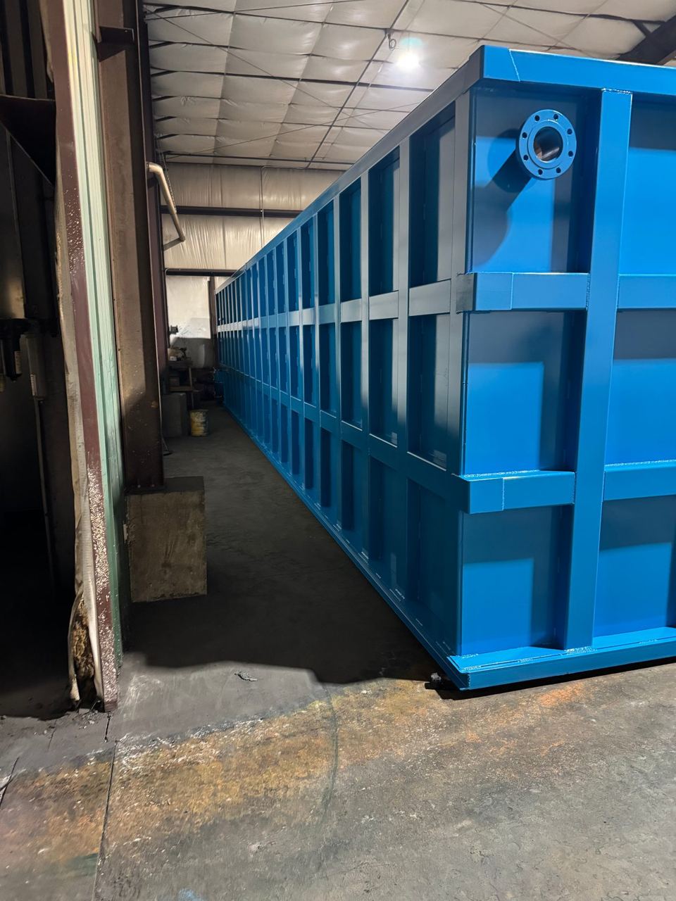 Blue modular steel tank running down a narrow shop aisle, top-corner flanged nozzle in the foreground