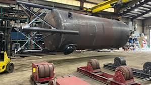 Cone-bottom shop-welded round steel tank supported on turning rolls inside the fabrication shop