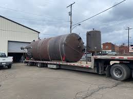 Finished shop-welded round steel tank strapped to a flatbed trailer outside the fabrication shop, ready to ship complete