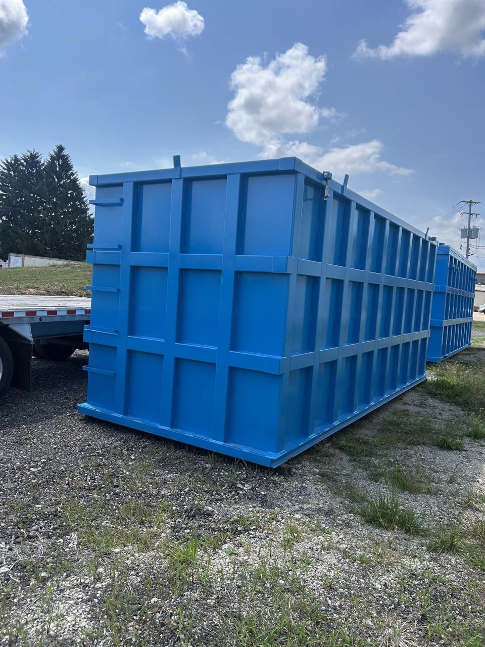 Bright blue shop-welded steel tank staged outdoors on gravel, externally reinforced panel grid facing the camera