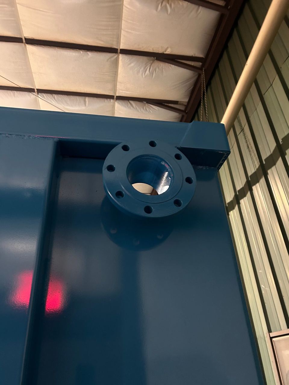 Detail of a bolt-pattern flanged nozzle welded to the top corner of a dark blue shop-welded steel tank in the shop