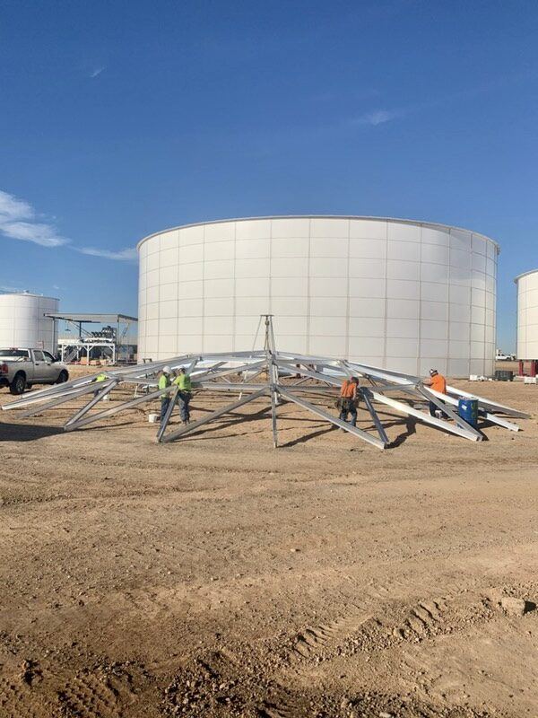 Finished white storage tank with aluminum cover components staged beside the installation area