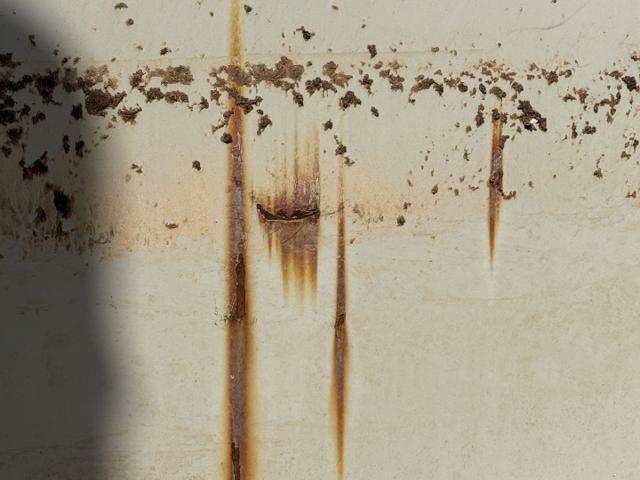 Rust streaks running down a white tank shell from a corroding bolted seam
