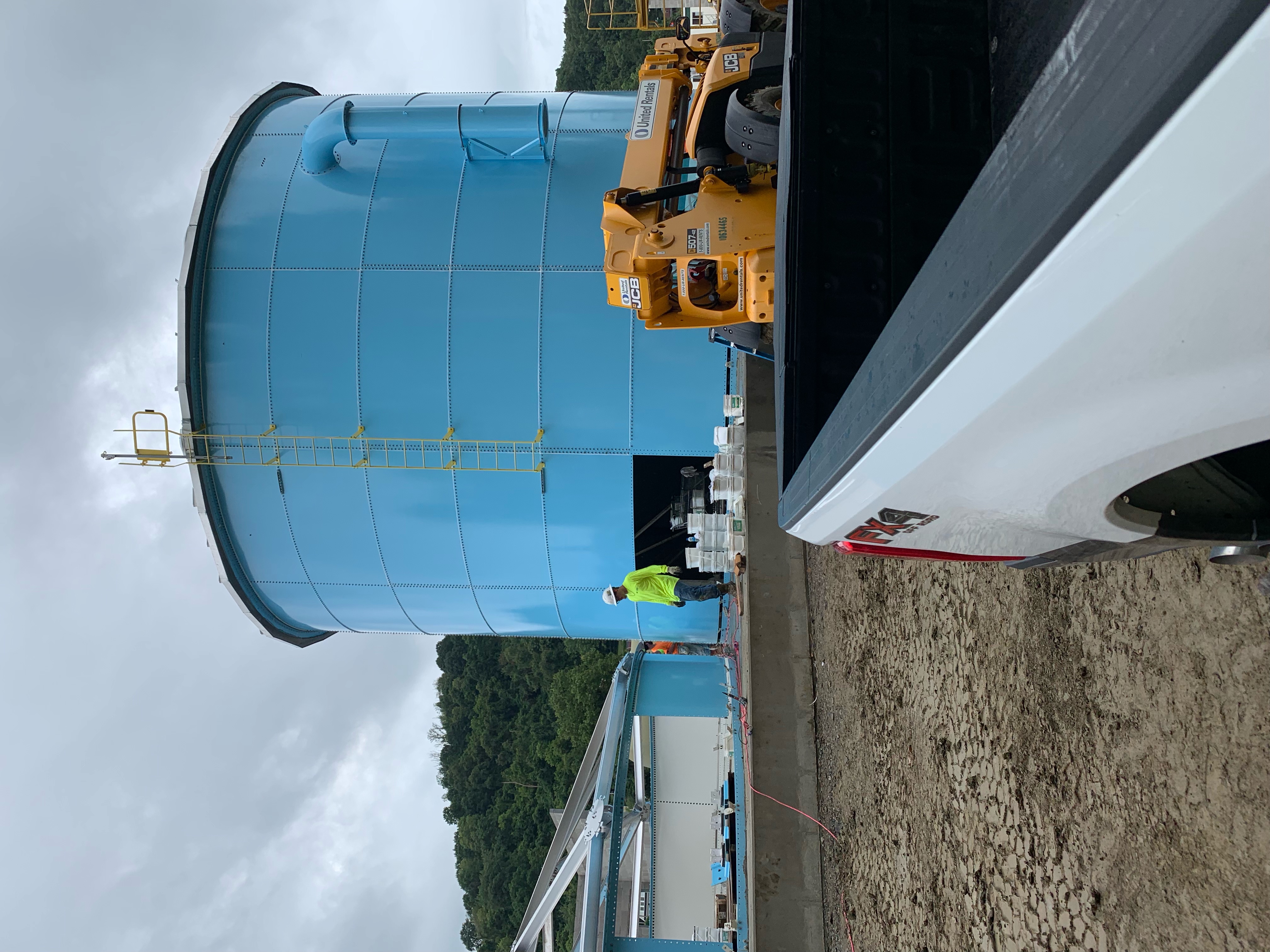 Blue bolted steel tank under construction with a telehandler positioning roof structure