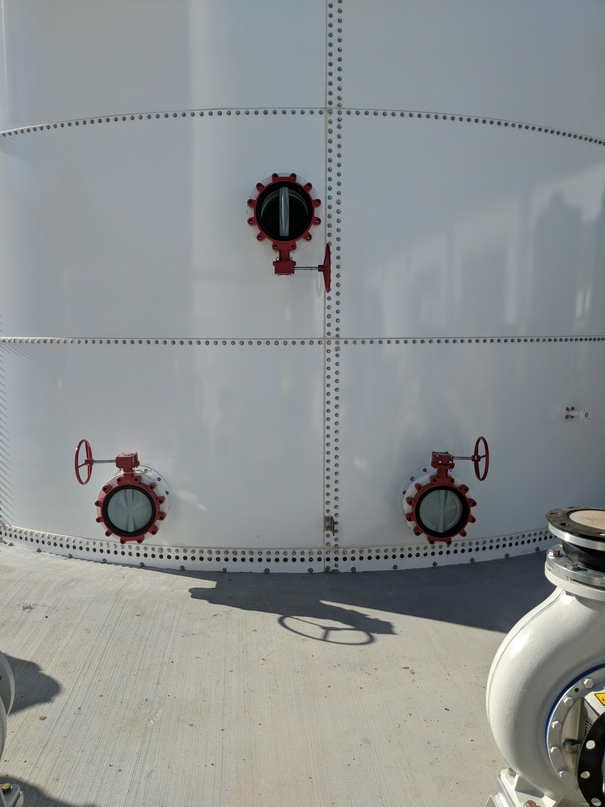 Close-up of red butterfly valves mounted on the white bolted panel wall of a steel tank