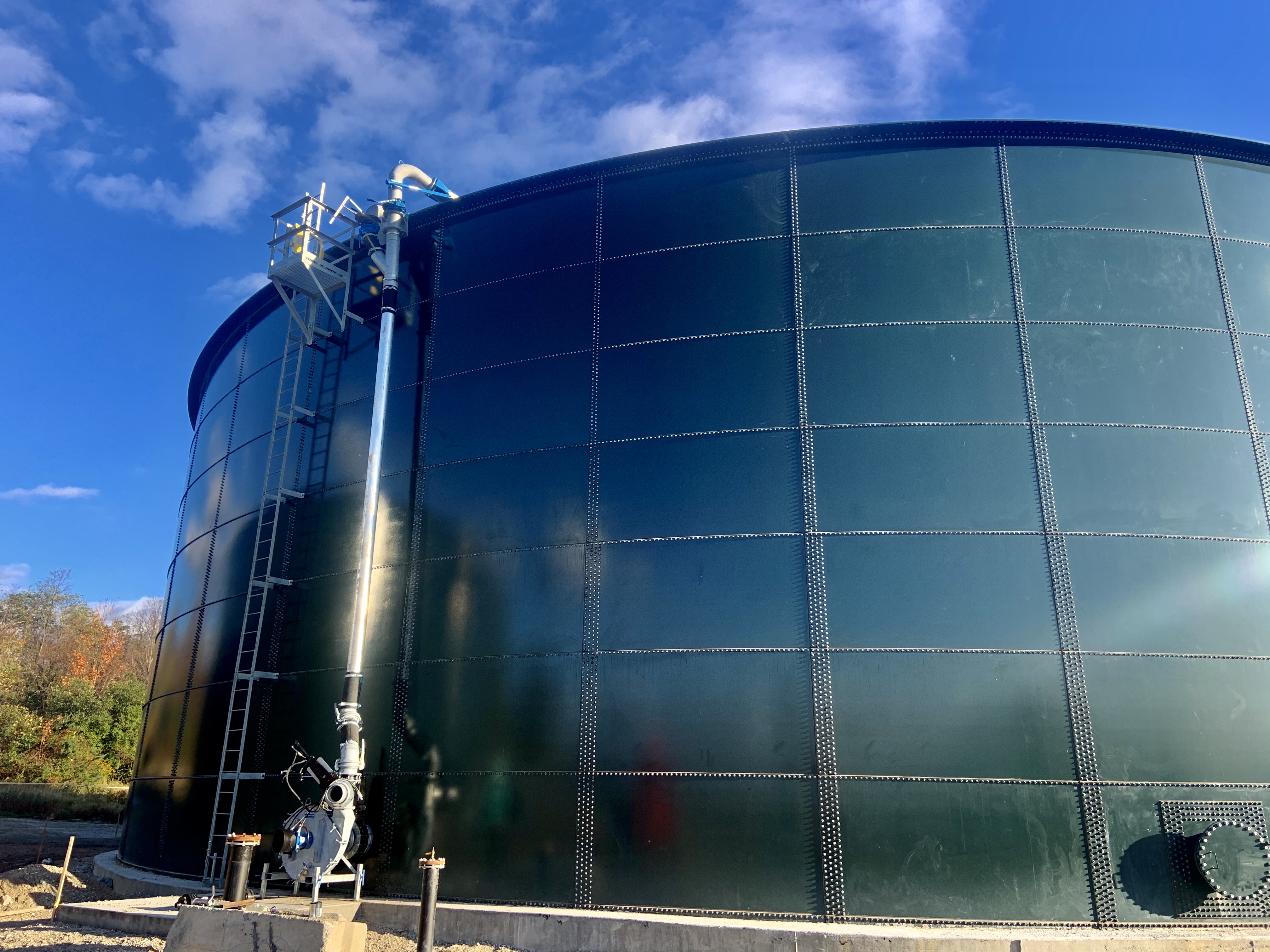 Completed fusion-bonded epoxy bolted steel tank with side-mounted piping against a clear sky