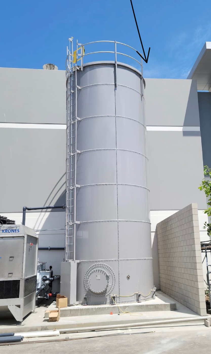 Tall grey bolted steel process tank installed between two industrial buildings