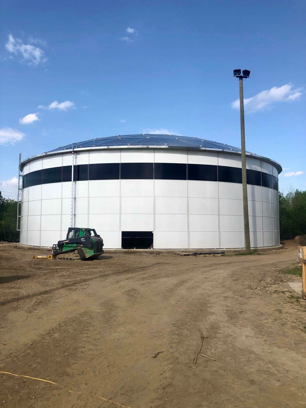 White bolted steel tank with aluminum dome roof and a telehandler working at its base during construction