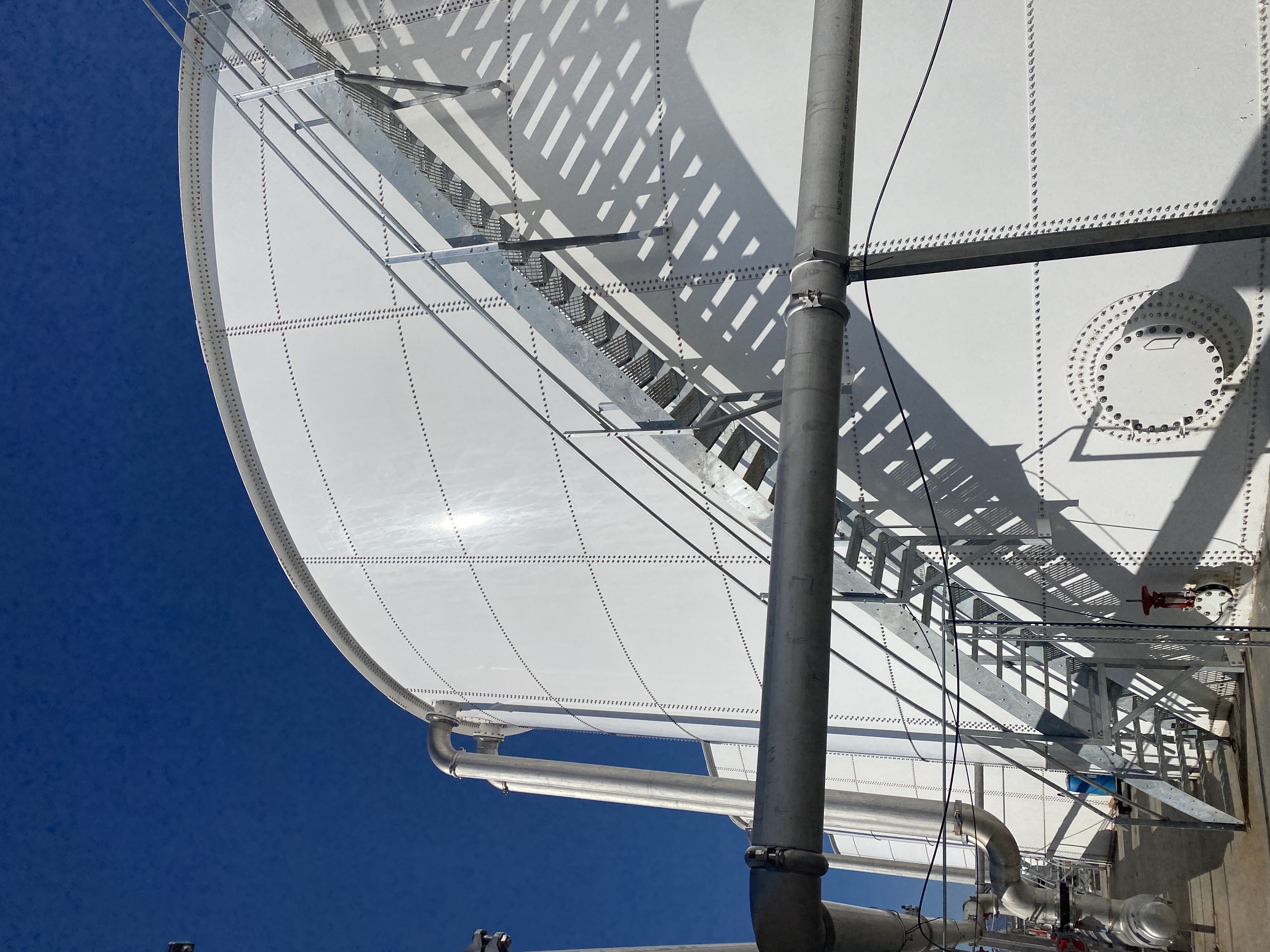 Upward view of a white bolted steel tank shell and roof against a deep blue sky