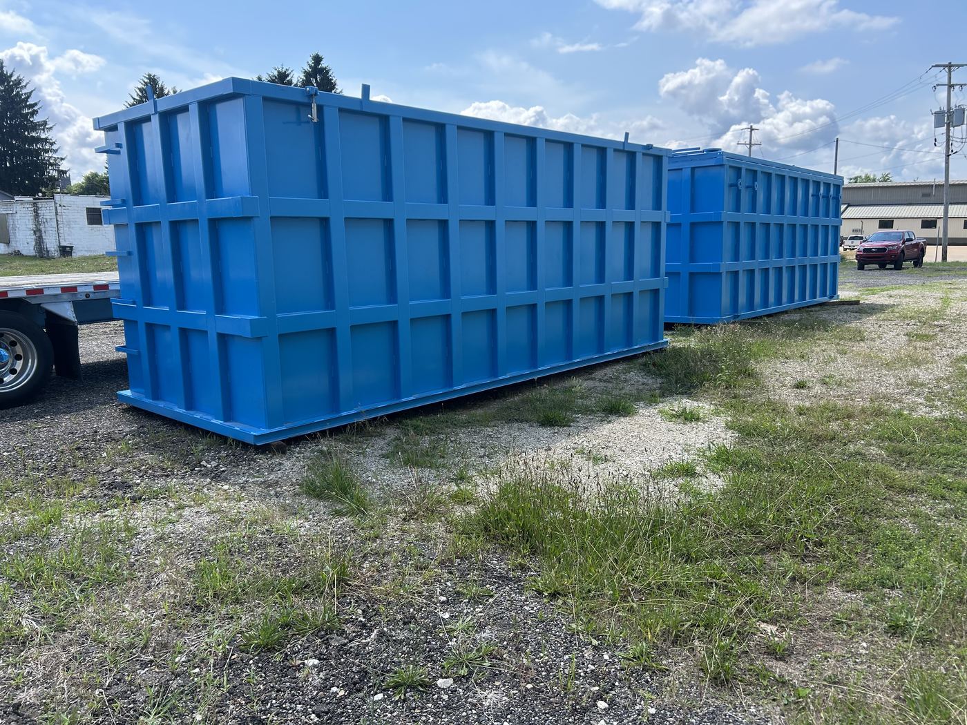 Pair of bright blue open-top modular steel tanks staged side by side in a grassy yard, externally reinforced panel walls under a clear sky